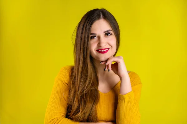 Portrait of a pretty brunette girl with long hair with a smile in a yellow sweater on a yellow background smiles and shows positive emotions — Stock Photo, Image