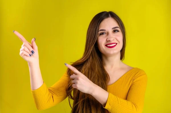 Menina morena agradável com cabelos longos com um sorriso em uma jaqueta amarela se alegra em um fundo amarelo, sorri e mostra emoções positivas — Fotografia de Stock