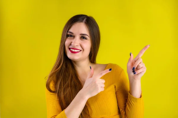 Menina morena agradável com cabelos longos com um sorriso em uma jaqueta amarela se alegra em um fundo amarelo, sorri e mostra emoções positivas — Fotografia de Stock