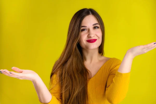 Menina morena agradável com cabelos longos com um sorriso em uma jaqueta amarela se alegra em um fundo amarelo, sorri e mostra emoções positivas — Fotografia de Stock