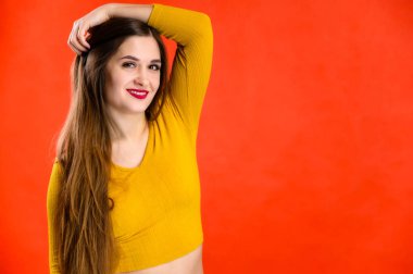 Sarı tişörtlü, uzun saçlı güzel esmer kız kırmızı arka planda gülümser ve olumlu duygular gösterir.