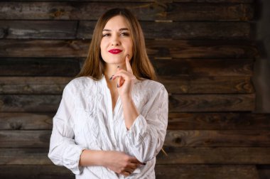 Uzun saçlı, beyaz tişörtlü hoş esmer kız ahşap arka planda iletişim kuruyor, gülümsüyor ve olumlu duygular gösteriyor.