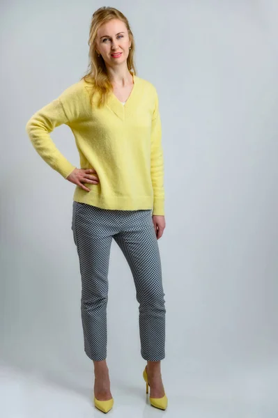 Полнометражный портрет стильной красивой блондинки в желтом свитере и серых брюках на белом фоне — стоковое фото