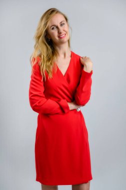 Kameranın önünde kırmızı elbiseli bir manken. Güzel bir kadının dikey portresi. 38 yaşında, beyaz arka planda, gülümseyen bir sarışın..