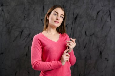 Gri arka planda pembe kazaklı güzel bir beyaz kadın konuşuyor ve anlatıyor..