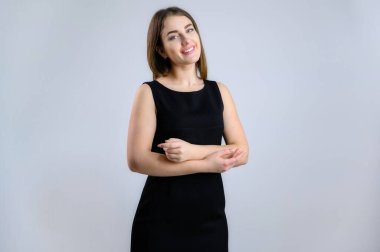 Güzel, beyaz bir kadının genel konsepti. Kameranın önünde duran siyah elbiseli bir manken beyaz arka planda gülümsüyor..