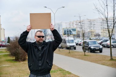 Sokakta elinde siyah ceketli, beyaz bir adamın resmi var. Akşamüstü.