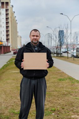 Sokakta elinde siyah ceketli, beyaz bir adamın resmi var. Akşamüstü.