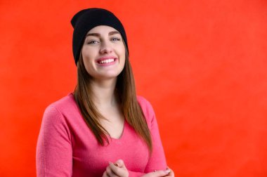 Güzel bir genç kadının portresi pembe bir kazakla gülüyor. Kırmızı bir arka planda neşeli duygularla.