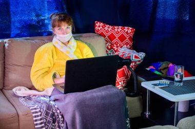 Evin içinde karantina altında maske takan bir kadının fotoğrafı. Model çalışıyor, internet üzerinden dizüstü bilgisayar kullanıyor..