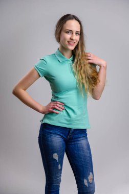 Evrensel bir kavram. Beyaz arka planda uzun saçlı, turkuaz tişörtlü ve kot pantolonlu güzel beyaz bir kadının dikey portresi. Gülümseyen bir manken