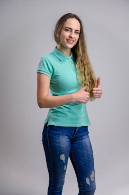 Evrensel bir kavram. Manken gülümsüyor ve beyaz arka planda turkuaz tişört ve mavi kot pantolon giyen uzun saçlı güzel beyaz bir kadının dikey portresini gösteriyor..