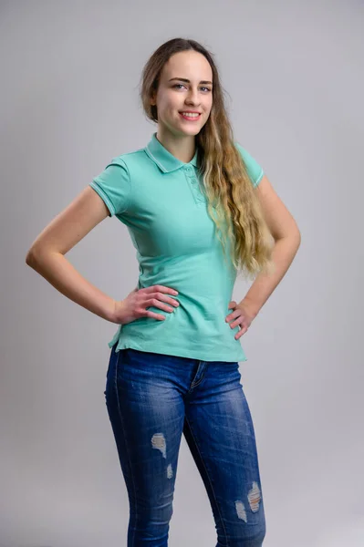 普遍的な概念 白い背景にターコイズのTシャツとブルーのジーンズに長い髪を持つかなり白人女性の垂直肖像画 モデルは笑顔で立っている — ストック写真