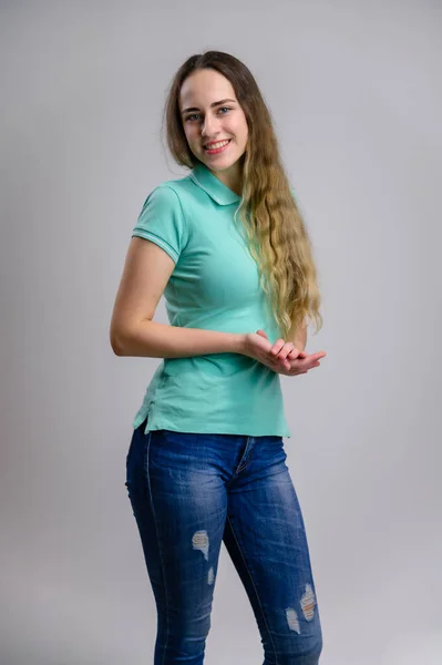 白い背景にターコイズブルーのジーンズのブラウスに長い髪をした笑顔のかなり若い女性の垂直写真 — ストック写真