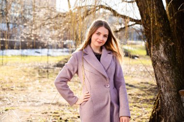 Güzel gülümseyen sarışın beyaz bir kızın portresi. Açık havada uzun güzel saçları var. Pembe bir ceketi var..