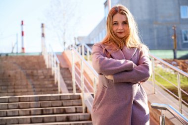 Güzel bir model poz vermekten mutluluk duyar. Güneşli bir günde binanın arka planında pembe ceketli, uzun, güzel saçlı, mutlu, beyaz bir kızın fotoğrafı..