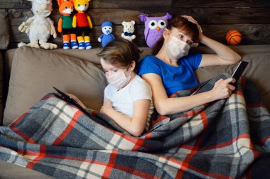 9 yaşındaki bir çocuğun evinde çekilmiş bir fotoğraf. Annesiyle birlikte tıbbi bir maskeyle kanepede yatıyor. Elinde telefon tableti karantinada.