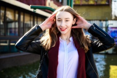 Baharda açık havada güneşte çekilmiş bir fotoğraf. Binanın arka planında duygularıyla gülümseyen güzel bir kız.