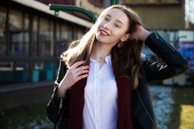 Baharda açık havada güneşte çekilmiş bir fotoğraf. Binanın arka planında duygularıyla gülümseyen güzel bir kız.