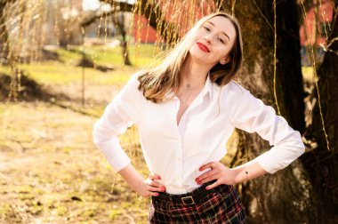 Güneşin altında duyguları olan gülümseyen güzel bir kızın bahar portresi. Model kameranın önünde beyaz bir bluz giyiyor.