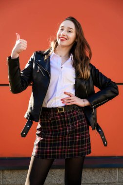 Portakal rengi arka planda, güneşte duyguları olan, gülümseyen güzel bir kızın dikey portresi. Kameranın önünde ellerinle poz ver..