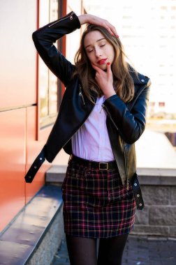 Şehrin arka planında, güneşin altında duyguları olan gülümseyen güzel bir kızın dikey bahar portresi. Kameranın önünde ellerinle poz ver..