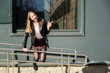 Şehrin arka planında, güneşte duyguları olan gülümseyen güzel bir kızın bahar portresi. Kameranın önünde ellerinle poz ver..