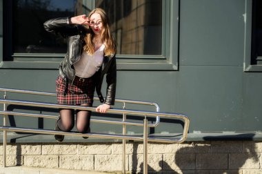 Şehrin arka planında, güneşin altında duyguları olan mutlu, gülümseyen güzel bir kızın bahar fotoğrafı. Kameranın önünde ellerinle poz ver..