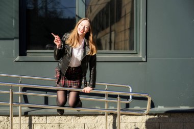 Şehrin arka planında, güneşin altında duyguları olan mutlu, gülümseyen güzel bir kızın bahar fotoğrafı. Kameranın önünde ellerinle poz ver..