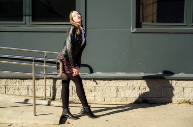 Şehrin arka planında, güneşin altında duyguları olan mutlu, gülümseyen güzel bir kızın bahar fotoğrafı. Kameranın önünde ellerinle poz ver..