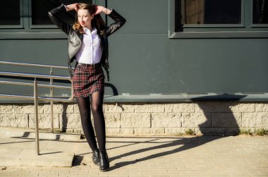 Şehrin arka planında, güneşin altında duyguları olan mutlu, gülümseyen güzel bir kızın bahar fotoğrafı. Kameranın önünde ellerinle poz ver..