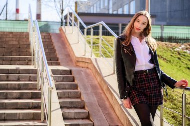 Şehrin arka planında, güneşin altında duyguları olan mutlu, gülümseyen güzel bir kızın bahar dikey fotoğrafı. Kameranın önünde poz veren güzel bir model..