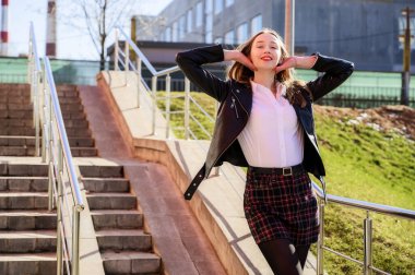 Şehrin arka planında, güneşin altında duyguları olan mutlu, gülümseyen güzel bir kızın bahar dikey fotoğrafı. Kameranın önünde poz veren güzel bir model..