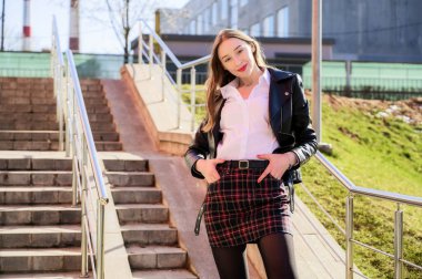 Şehrin arka planında, güneşin altında duyguları olan mutlu, gülümseyen güzel bir kızın bahar dikey fotoğrafı. Kameranın önünde poz veren güzel bir model..