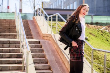 Şehrin arka planında, güneşin altında duyguları olan mutlu, gülümseyen güzel bir kızın bahar dikey fotoğrafı. Kameranın önünde poz veren güzel bir model..