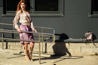 Güneşli bahar aylarında binanın arka planında uzun saçlı, şık ve alımlı güzel bir kadının parlak havasında çekilmiş bir fotoğraf..