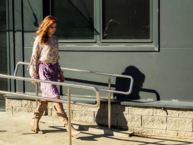 Güneşli bahar aylarında, binanın arka planında uzun saçlı, şık, alımlı, güzel bir kadının parlak havada çekilmiş uzun bir fotoğrafı..