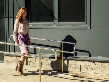 Güneşli bahar aylarında, binanın arka planında uzun saçlı, şık, alımlı, güzel bir kadının parlak havada çekilmiş uzun bir fotoğrafı..