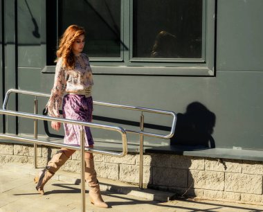 Güneşli bahar aylarında, binanın arka planında uzun saçlı, şık, alımlı, güzel bir kadının parlak havada çekilmiş uzun bir fotoğrafı..