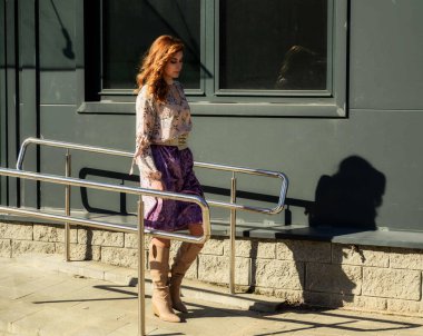 Güneşli bahar aylarında, binanın arka planında uzun saçlı, şık, alımlı, güzel bir kadının parlak havada çekilmiş uzun bir fotoğrafı..