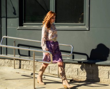 Güneşli bahar aylarında, binanın arka planında uzun saçlı, şık, alımlı, güzel bir kadının parlak havada çekilmiş uzun bir fotoğrafı..