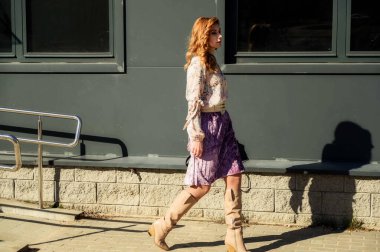 Şık, alımlı, güzel bir kadının tam boy fotoğrafı. Arka planda uzun saçları olan. Baharda güneşin altında, binanın merdivenlerinde..