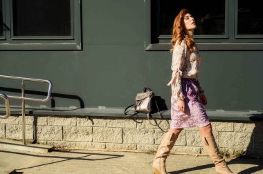 Şık, alımlı, güzel bir kadının tam boy fotoğrafı. Arka planda uzun saçları olan. Baharda güneşin altında, binanın merdivenlerinde..