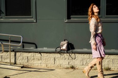 Şık, alımlı, güzel bir kadının tam boy fotoğrafı. Arka planda uzun saçları olan. Baharda güneşin altında, binanın merdivenlerinde..