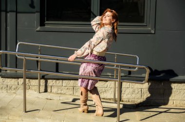 Şık, alımlı, güzel bir kadının tam boy fotoğrafı. Arka planda uzun saçları olan. Baharda güneşin altında, binanın merdivenlerinde..