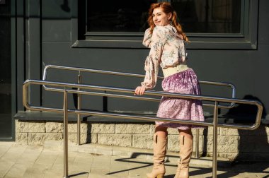 Şık, alımlı, güzel bir kadının tam boy fotoğrafı. Arka planda uzun saçları olan. Baharda güneşin altında, binanın merdivenlerinde..