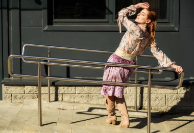 Güzel, modaya uygun, uzun saçlı bir kadının tam boy fotoğrafı. Baharda, güneşli bir havada, bir binanın arka planında..