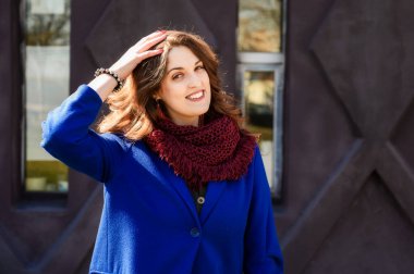 Oldukça şık esmer bir kadının portresi. Uzun, güzel saçlı, mavi ceketli, bir bina duvarında.