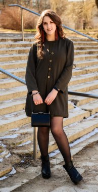 Güneşli bir havada binanın merdivenlerinin arkasında uzun ve güzel saçlı güzel bir esmer kadının portresi.