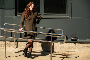 Şık, mutlu, uzun, güzel saçlı bir esmer kadının fotoğrafı. Şehrin arka planında, güneşli bir havada binanın merdivenlerinde, takım elbiseli bir kadın.